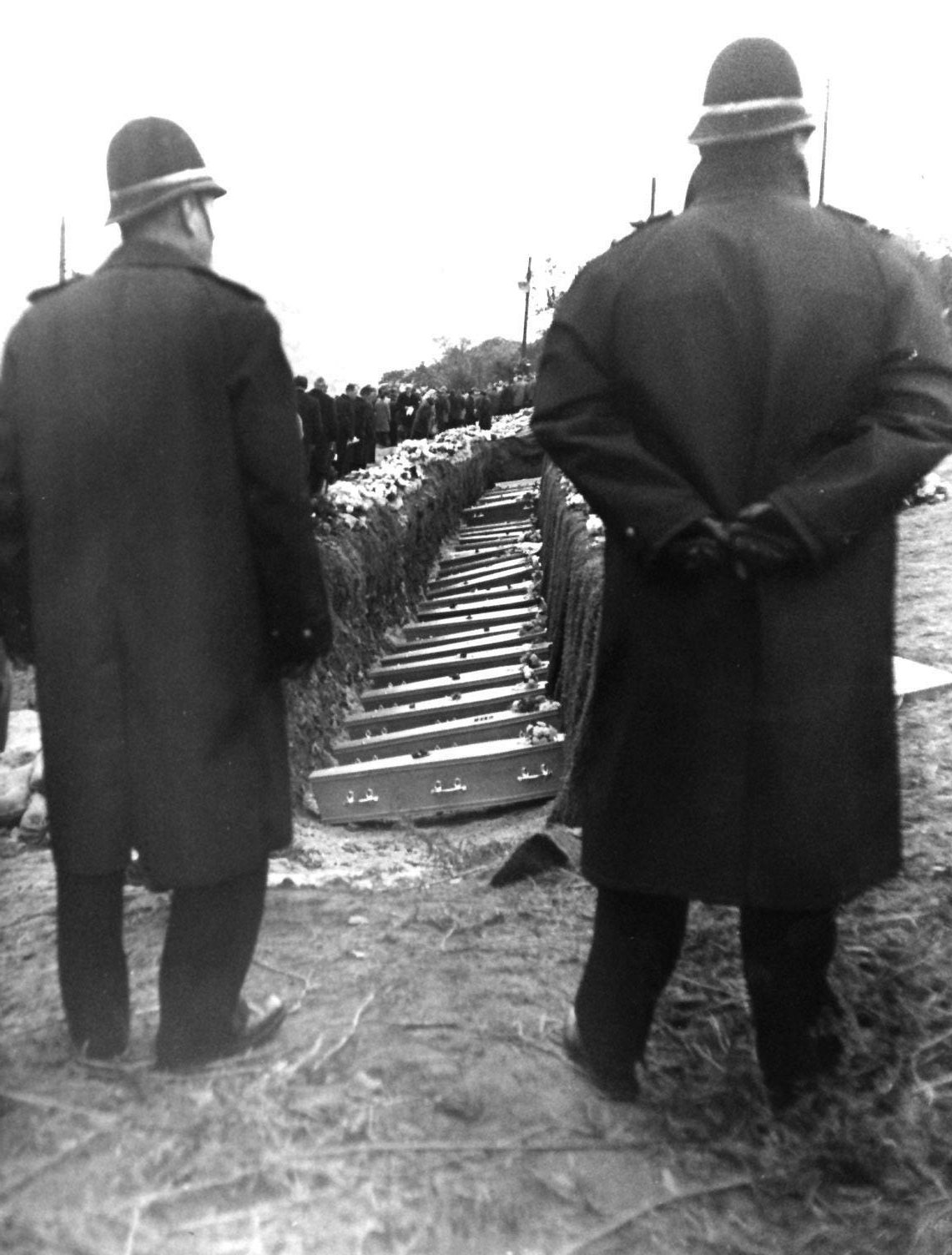 Library file 124814-63 dated 27/10/66: Between the figures of the guardian policeman the sad row of small coffins rests in the common grave in a hillside cemetery above Aberfan South Wales. 79 of the 116 children and one  of the 28 adults, a woman, victim